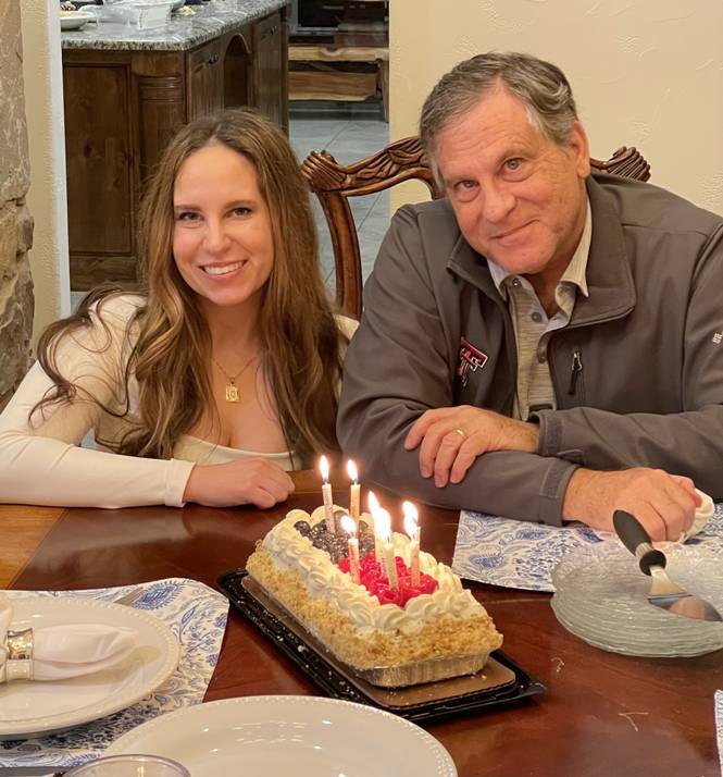 A person and person sitting at a table with a cake with candles

Description automatically generated